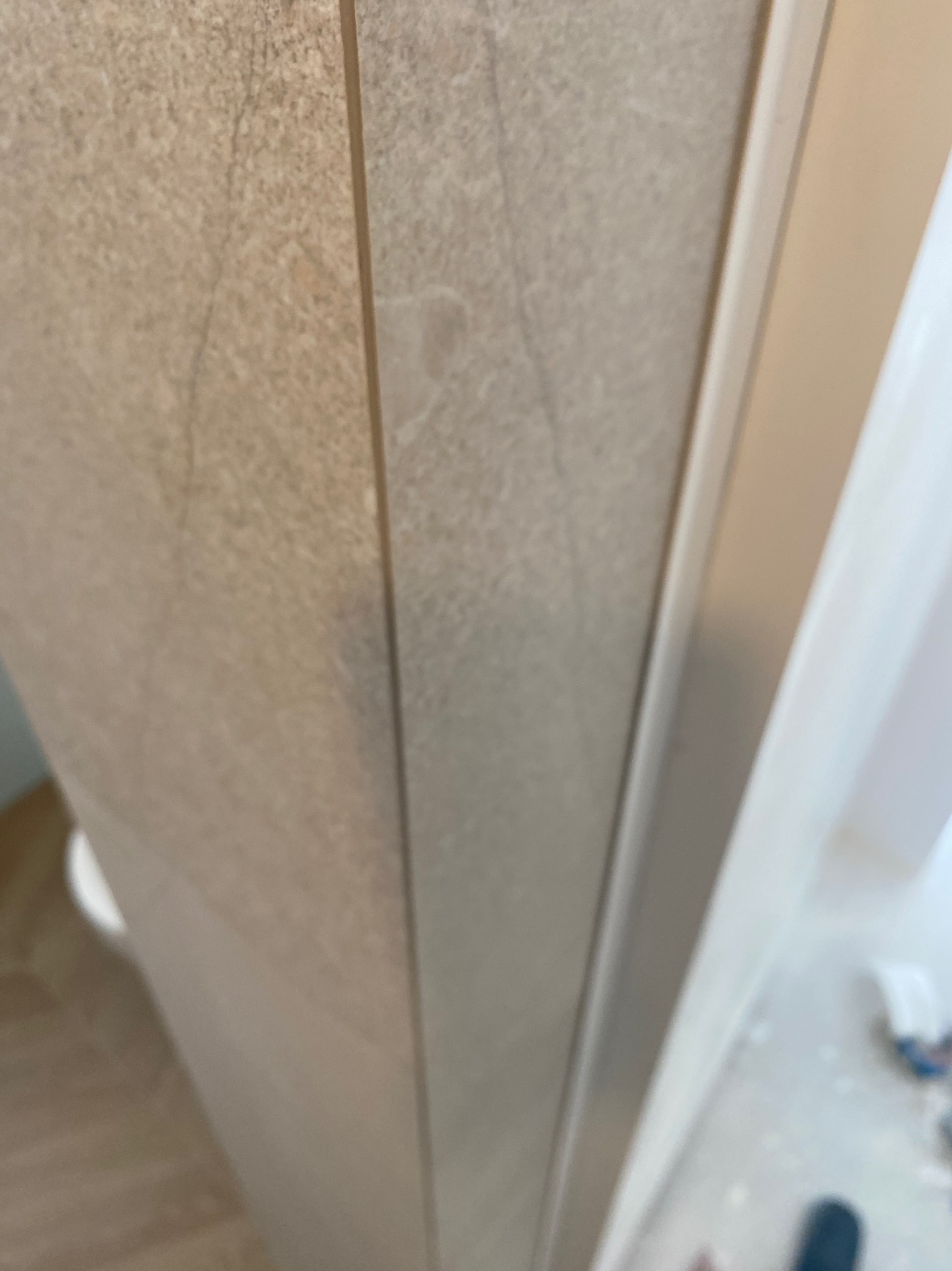 Beżowe płytki imitujące kamień na ścianie, widoczny fragment fugi i narożnika, niedokończone wykończenie łazienki.