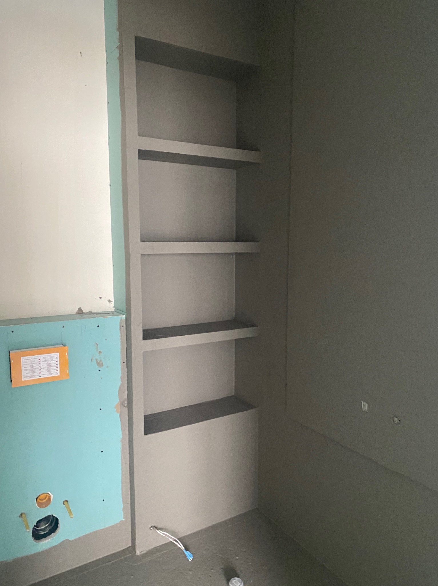 Wnęka z półkami w surowym stanie w łazience, ściany przygotowane pod malowanie, widoczne elementy instalacji hydraulicznej na ścianie z płyt gipsowych.