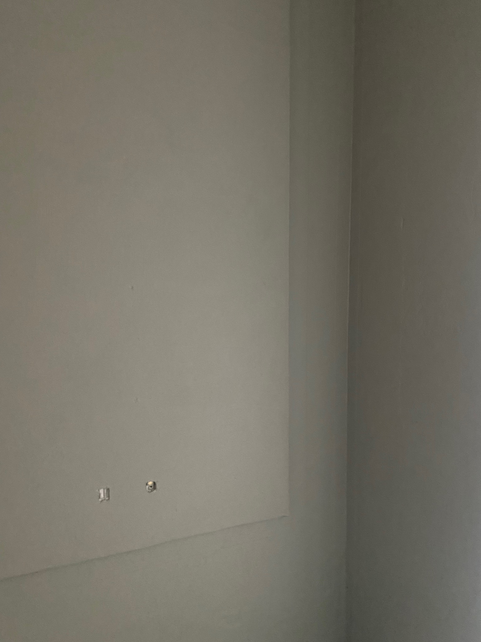 Szara ściana w rogu pomieszczenia, widoczne dwa otwory instalacyjne, przygotowana do dalszych prac wykończeniowych.