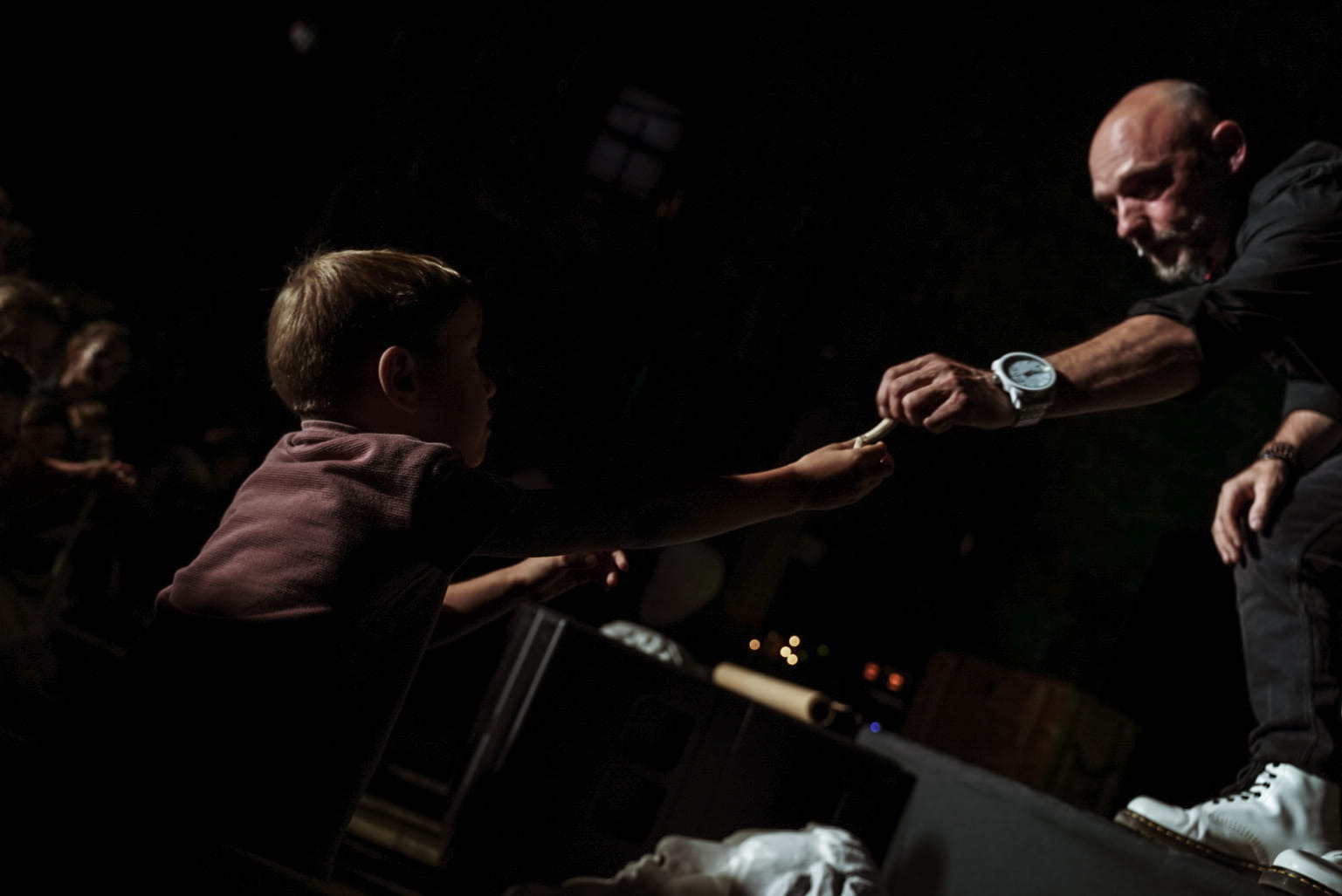 Iluzjonista w białych butach przekazuje rekwizyt dziecku na scenie w ciemnym otoczeniu, podczas występu.