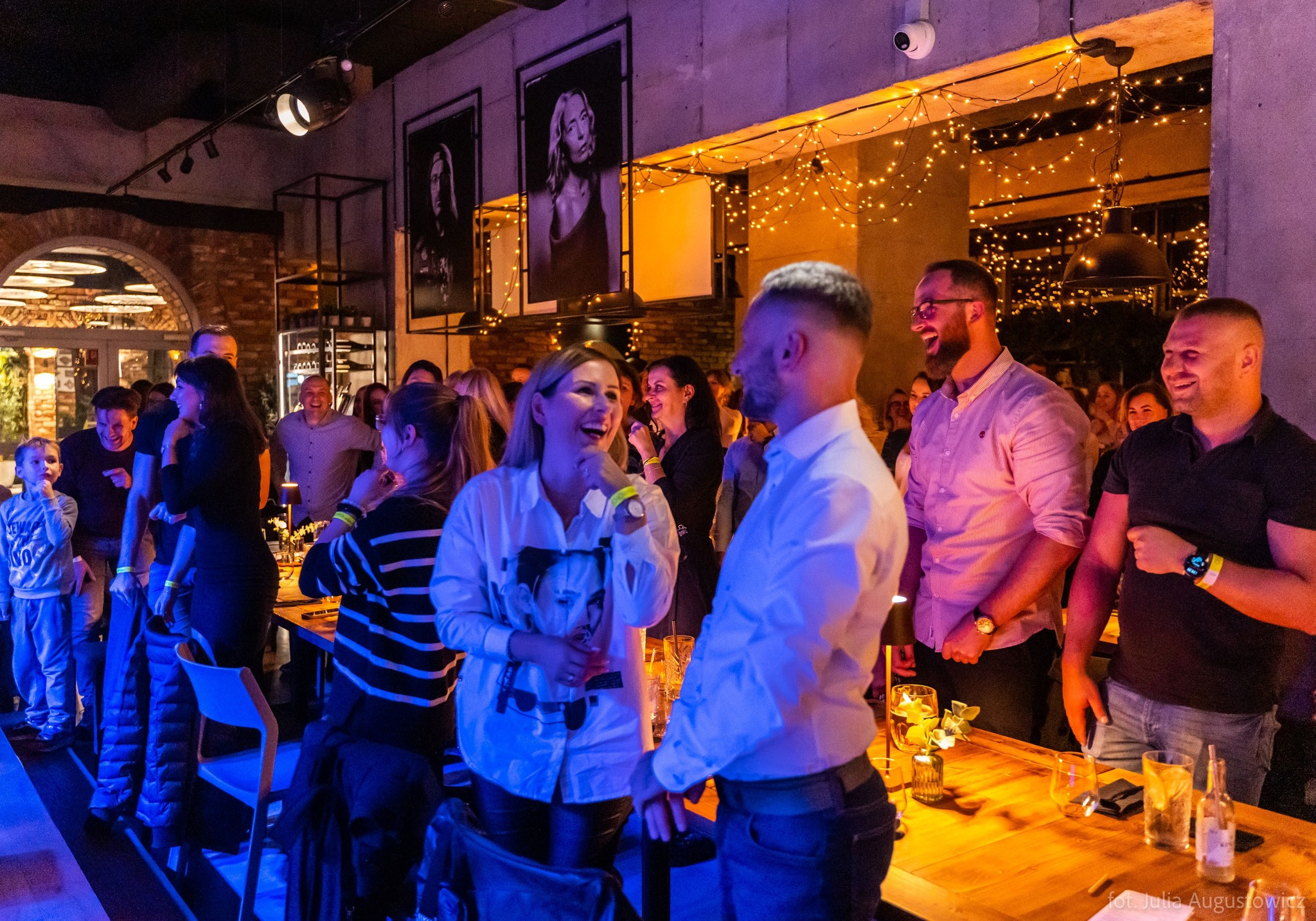 Rozbawieni goście w Gliwicach podczas imprezy w lokalu z dekoracyjnym oświetleniem i portretami na ścianach.