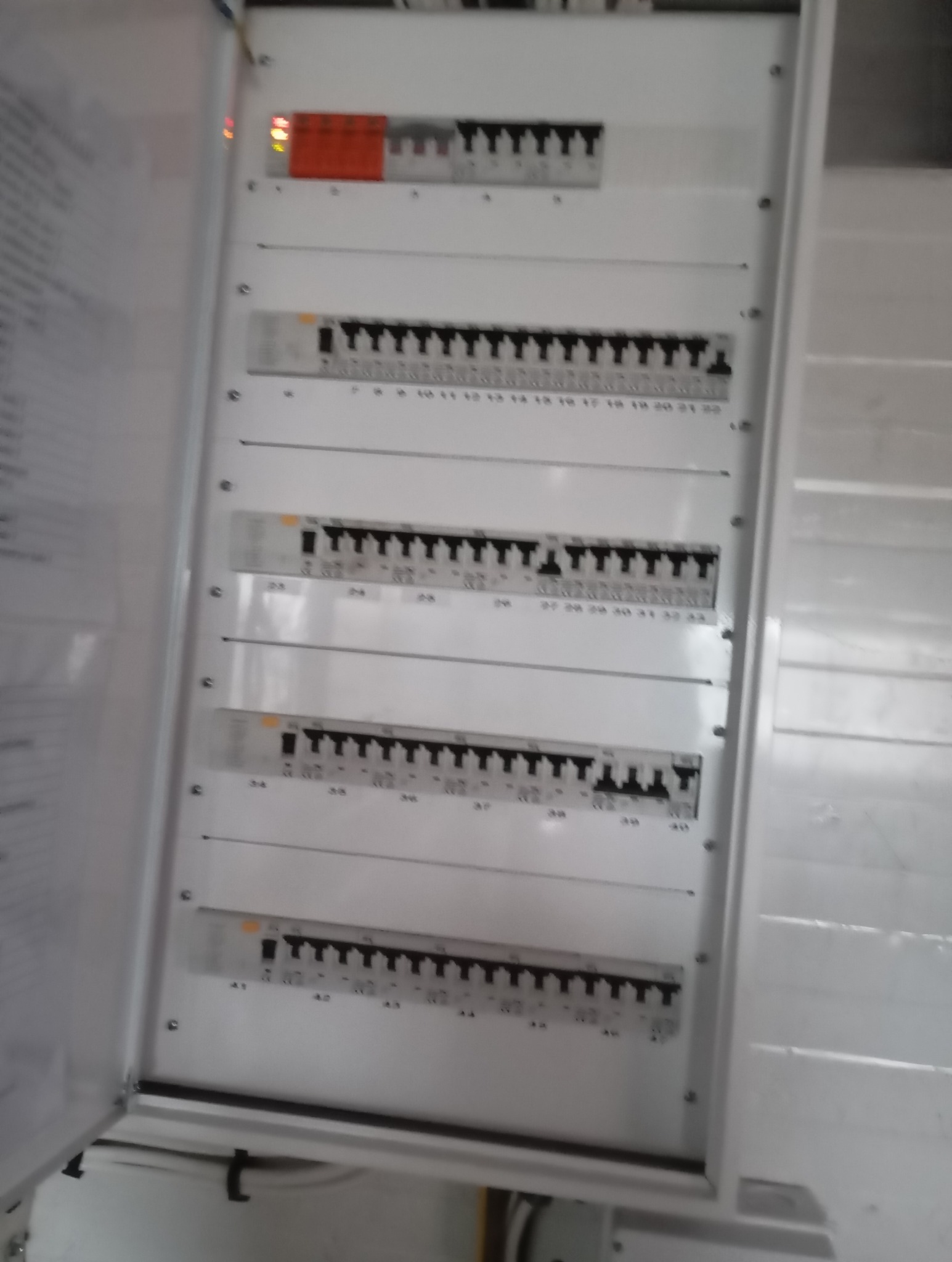 Otwarta skrzynka elektryczna z bezpiecznikami, widoczne oznaczenia numerów bezpieczników, w tle fragment dokumentacji.