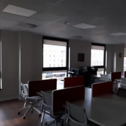 Biuro z widokiem na tory kolejowe przez okna z zasłoniętymi roletami w jasny dzień.