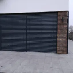 Zewnętrzne, poziome osłony okienne w kolorze grafitowym, zamontowane na nowoczesnym budynku z drewnianą okładziną, widoczne z poziomu szarego chodnika.