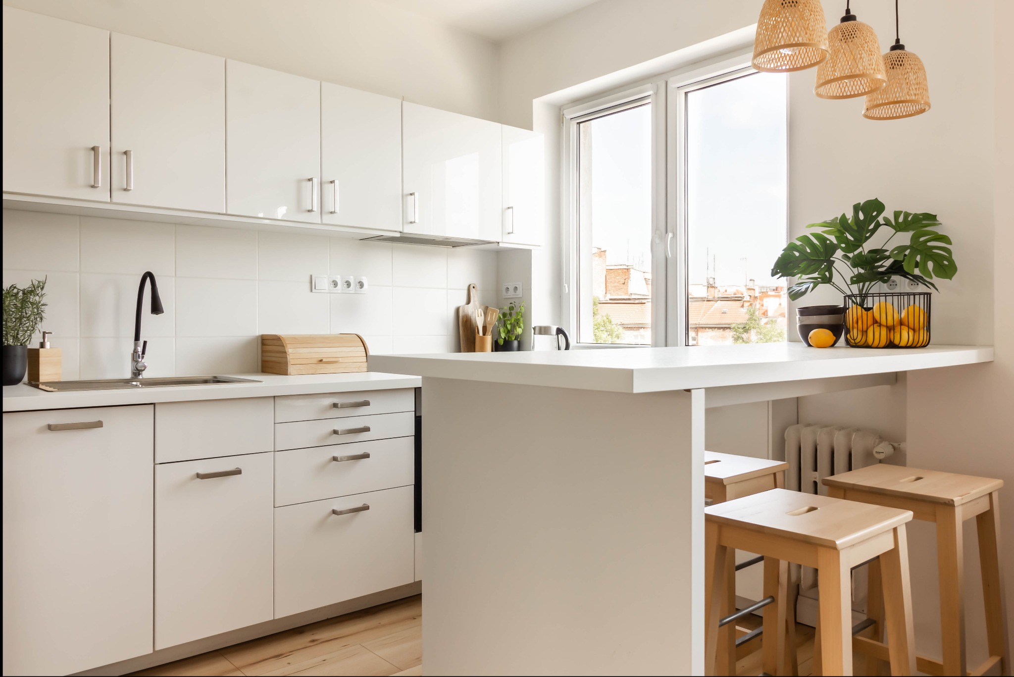 Jasna, nowoczesna kuchnia z białymi szafkami, drewnianymi hokerami przy blacie i widokiem na miasto z okna.