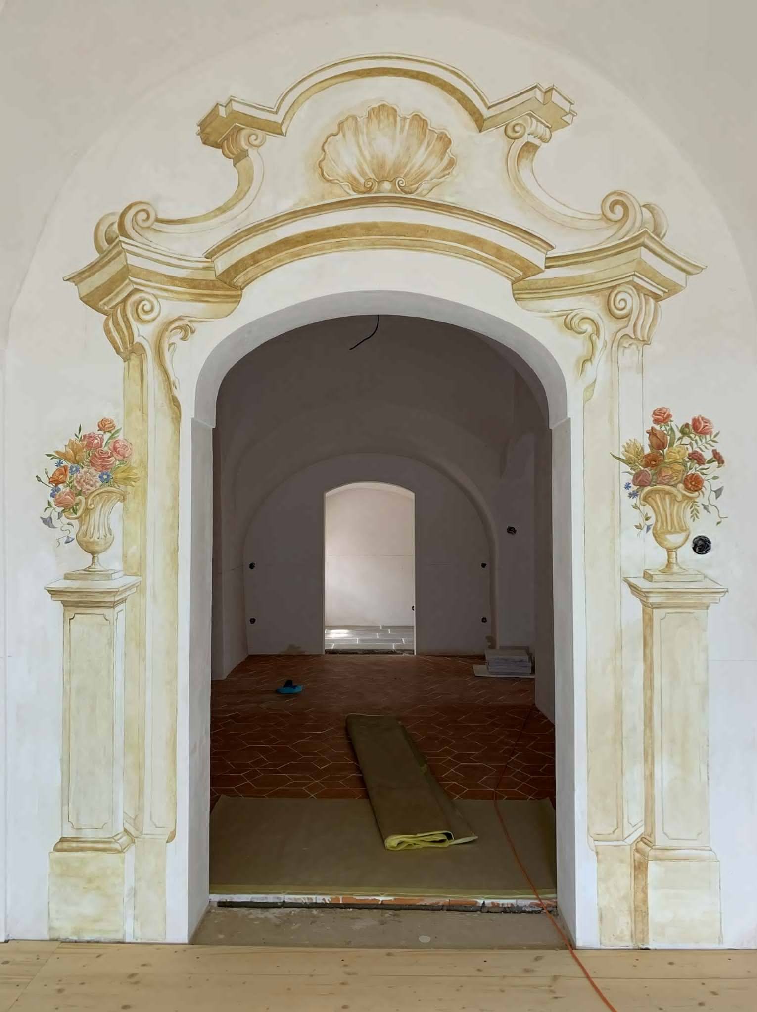 Ozdobne malowidła na ścianach i łuku przejścia, imitujące kolumny i wazony z kwiatami. Dekoracyjne wykończenie wnętrza w stylu klasycznym, z terakotową podłogą.