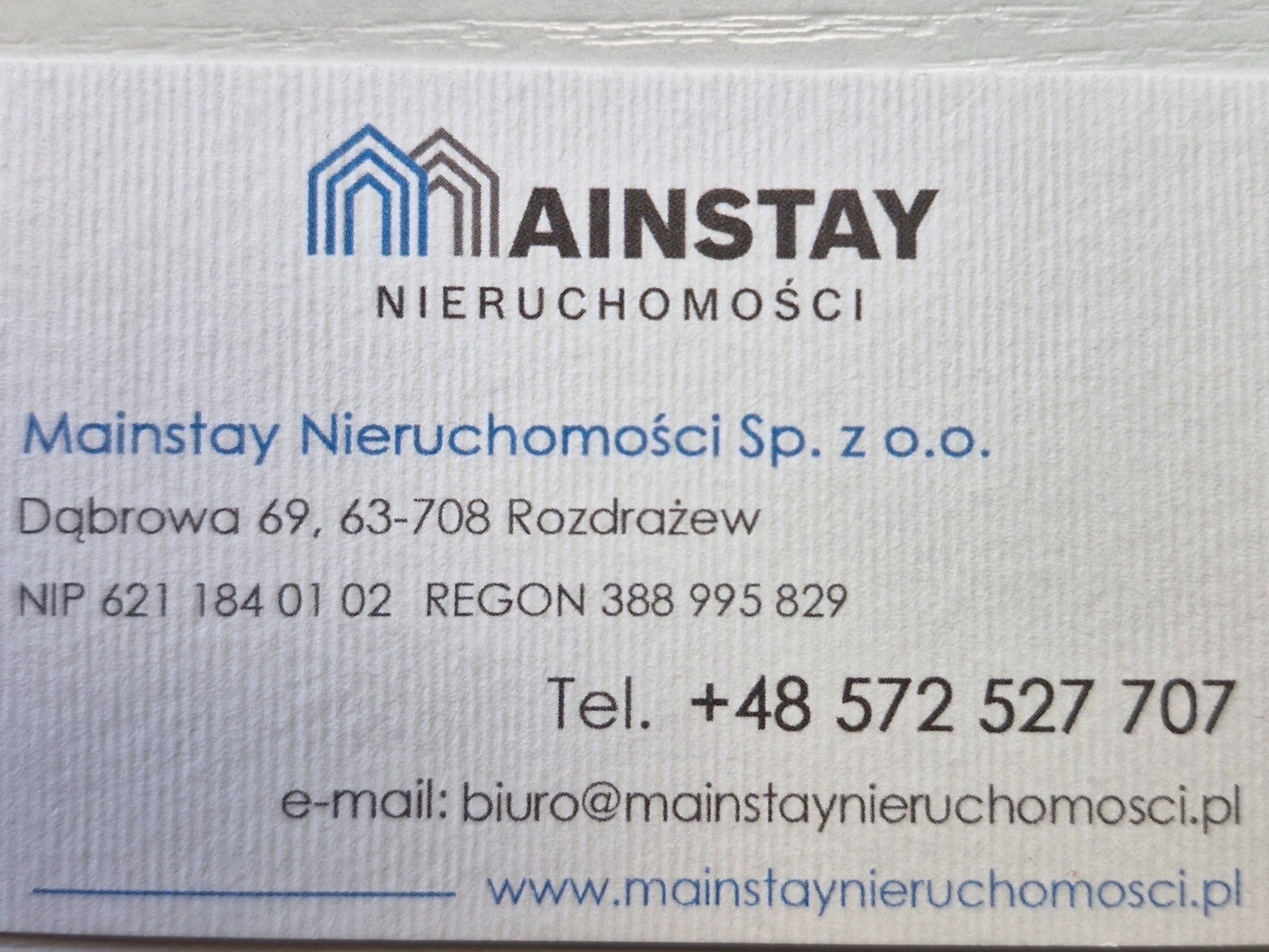 Wizytówka firmy Mainstay Nieruchomości z logo przedstawiającym schematyczny rysunek dwóch domów.