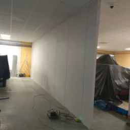 Montaż ścian działowych z płyt karton-gips w biurze. Widoczny laser krzyżowy, przewody i narzędzia. Część pomieszczenia zakryta folią malarską.