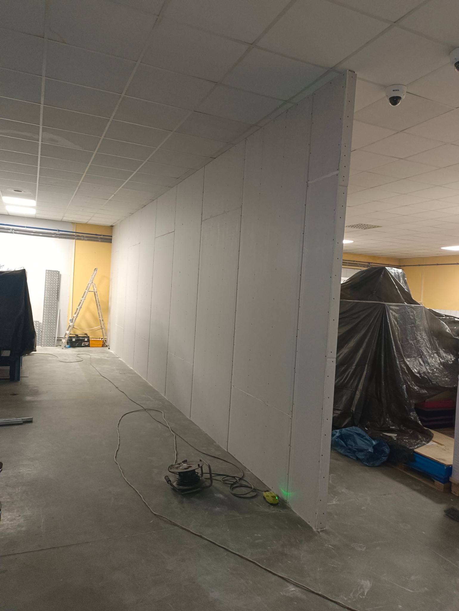 Montaż ścian działowych z płyt karton-gips w biurze. Widoczny laser krzyżowy, przewody i narzędzia. Część pomieszczenia zakryta folią malarską.