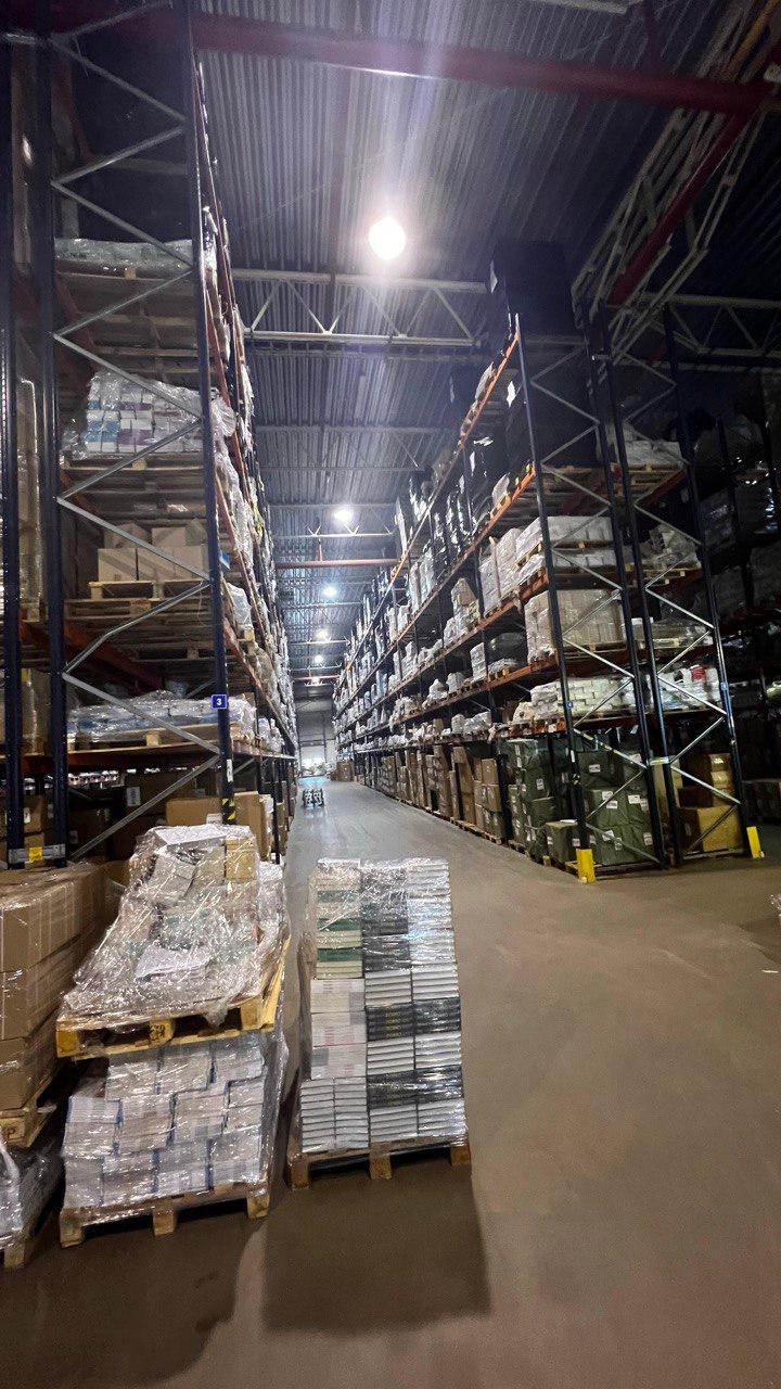 Magazyn wysokiego składowania z paletami towarów owiniętych folią stretch, widok w perspektywie w głąb hali.