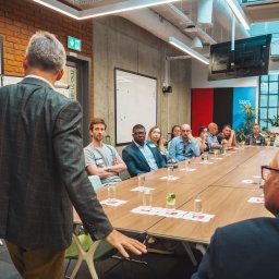 BOLD MEDIA SPÓŁKA Z OGRANICZONĄ ODPOWIEDZIALNOŚCIĄ - Sala konferencyjna podczas Polish Tech Day: Grupa osób siedzi przy długim stole, słuchając prezentacji; widoczne szklanki z wodą i logo wydarzenia w tle.