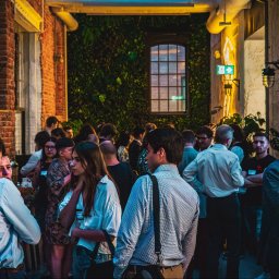 BOLD MEDIA SPÓŁKA Z OGRANICZONĄ ODPOWIEDZIALNOŚCIĄ - Fotorelacja z wydarzenia Polish Tech Day: tłum ludzi w przestrzeni z ceglaną ścianą, ścianą z roślin, oświetleniem neonowym i ekranem wyświetlającym zasady networkingu.