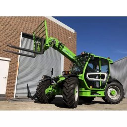 P.H. Agroma S.A. w Poznaniu - Zielona ładowarka teleskopowa Merlo TF35.7 na tle ceglanego budynku z zamkniętą bramą rolowaną, widok z boku, czyste niebo w tle.