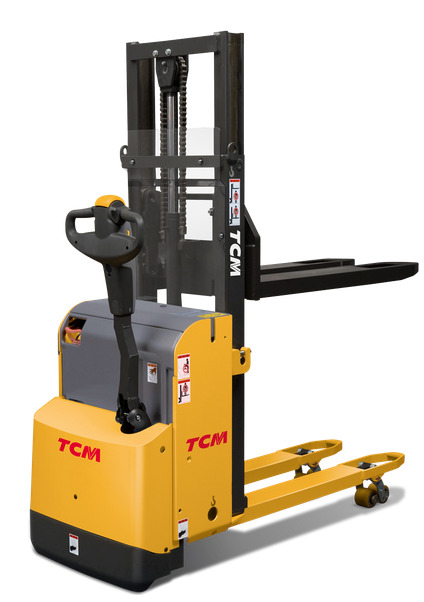 Żółto-szary wózek paletowy elektryczny marki TCM na białym tle, widok z boku. Widoczna konstrukcja masztu z łańcuchem i zabezpieczeniem, dyszel sterujący i palety.