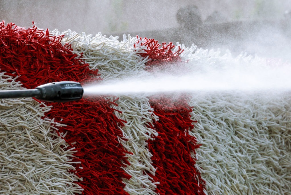 Czerwono-biały dywan shaggy czyszczony pod ciśnieniem z bliska, widoczna dysza spryskująca wodą.
