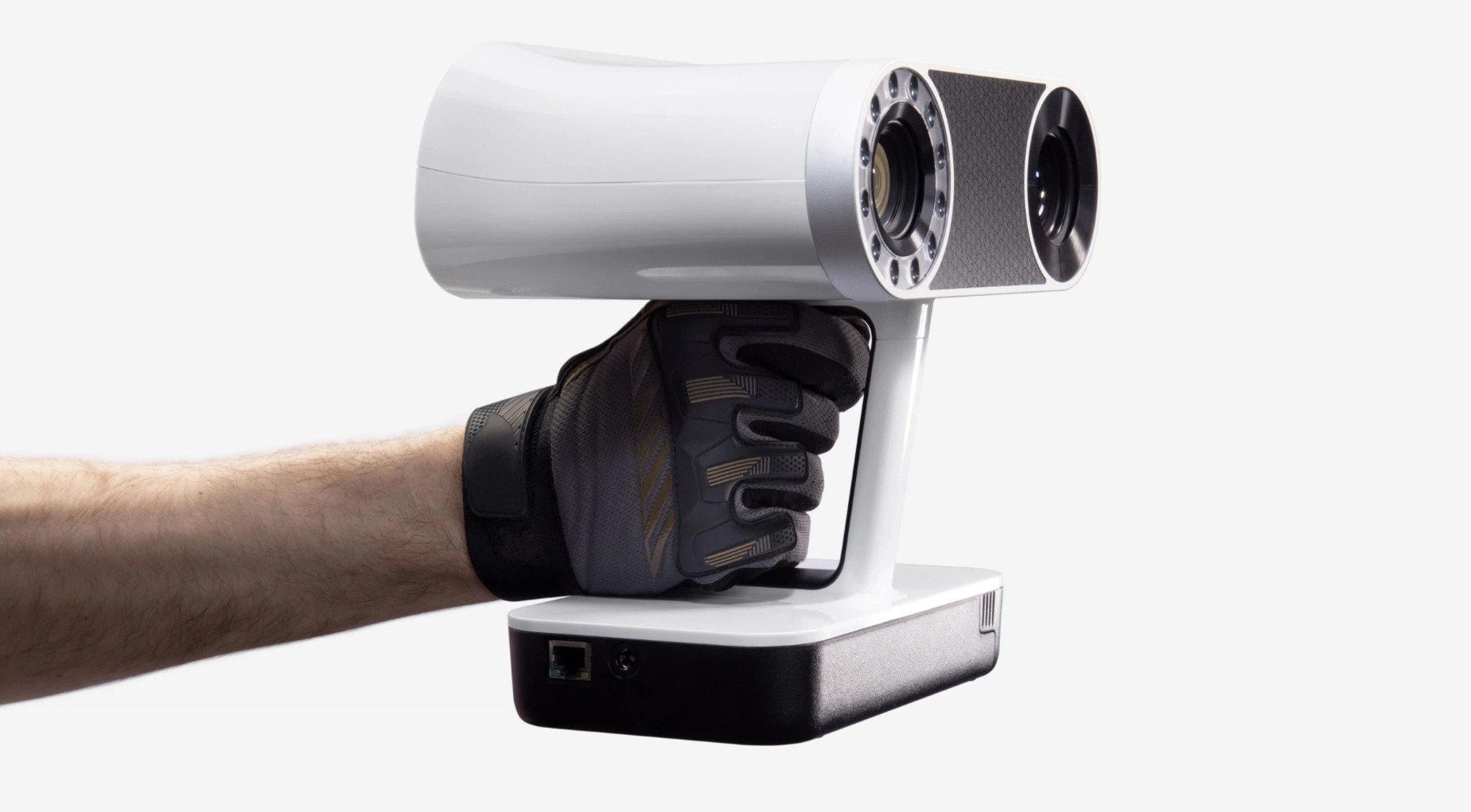 Ręka w rękawicy trzyma biały skaner 3D z dwoma obiektywami na białym tle.