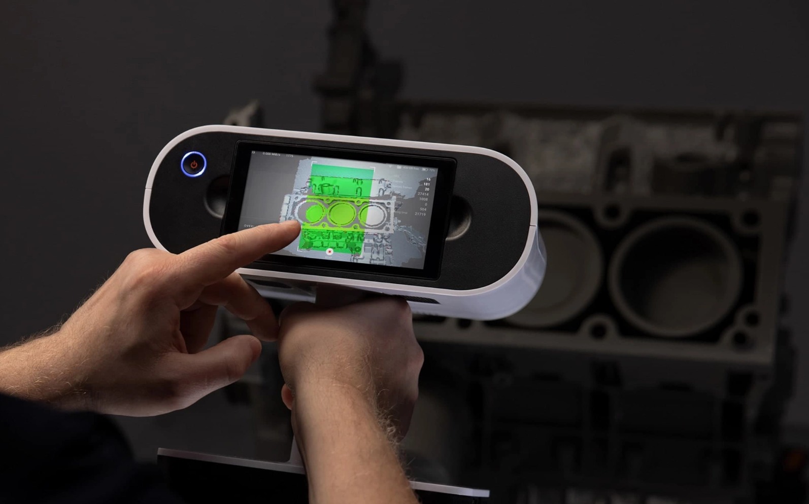 Skanowanie 3D bloku silnika za pomocą ręcznego skanera z ekranem dotykowym, wyświetlającym model z zaznaczonymi obszarami w kolorze zielonym.