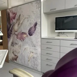 Wnętrze gabinetu stomatologicznego z nowoczesnym wyposażeniem, urządzeniem do zabiegów, biurkiem z komputerem i ścianą ozdobioną motywem piór