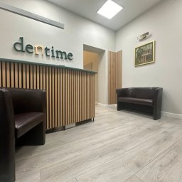 Studio Stomatologii Estetycznej DENTIME Jarosław - Recepcja w nowoczesnej klinice dentystycznej z drewnianą ladą, logo 'dentime' i skórzaną sofą w poczekalni.