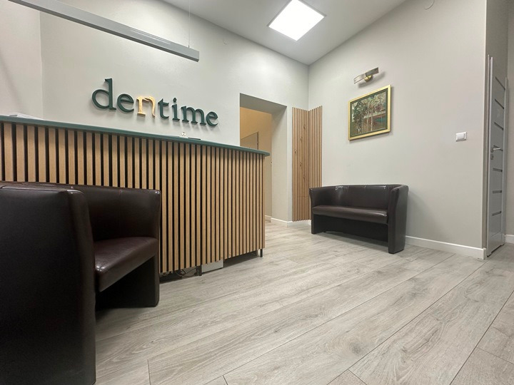 Recepcja w nowoczesnej klinice dentystycznej z drewnianą ladą, logo 'dentime' i skórzaną sofą w poczekalni.