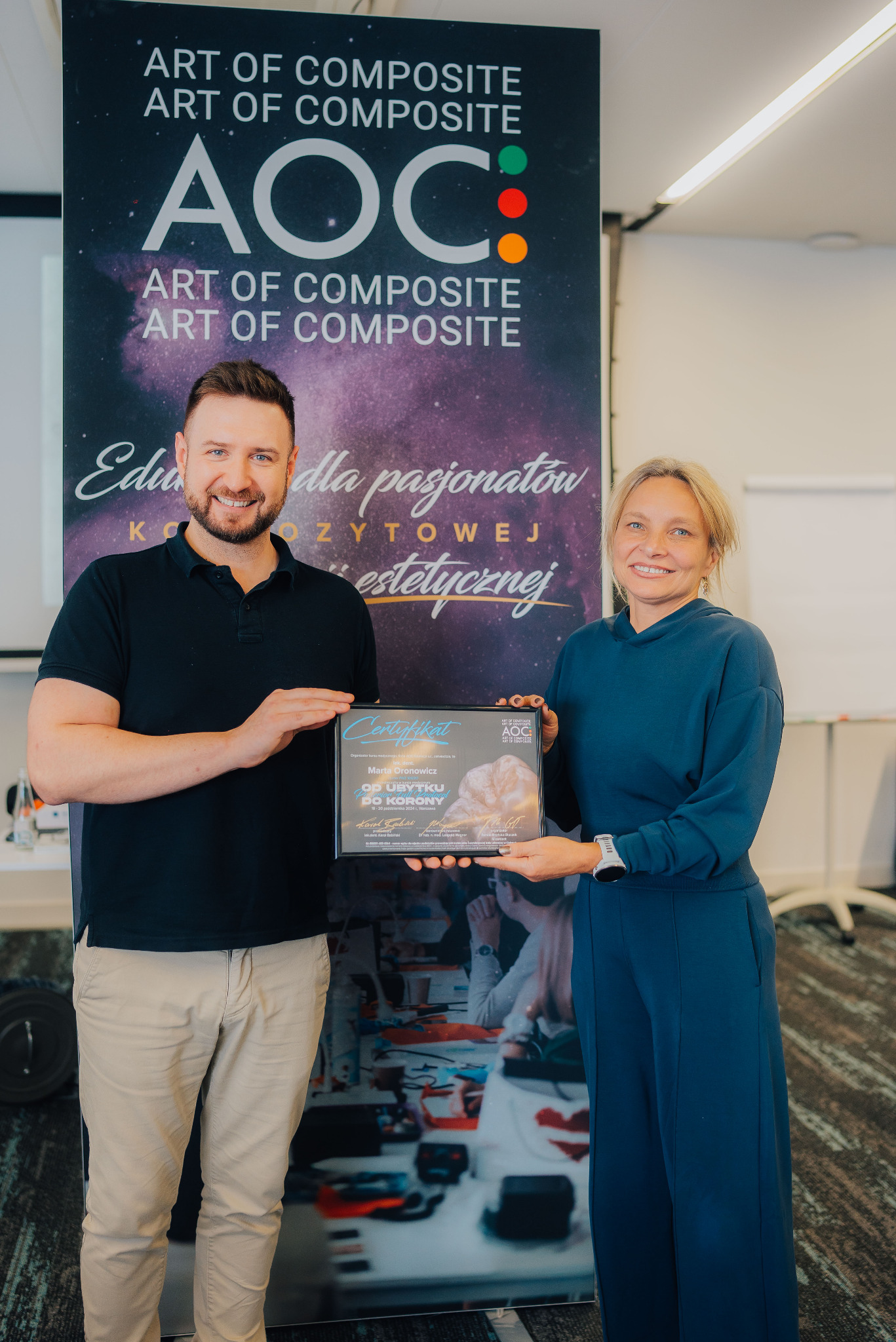 Dwie osoby prezentują certyfikat ukończenia kursu 'Od ubytku do korony' na tle baneru z napisem 'Art of Composite'.
