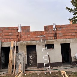 Firma Budowlana Bartłomiej Kierat - Wznoszenie ścian z czerwonej ceramiki poryzowanej na parterowym budynku, widoczna drabina oparta o ścianę, zbrojenie pionowe w spoinach.