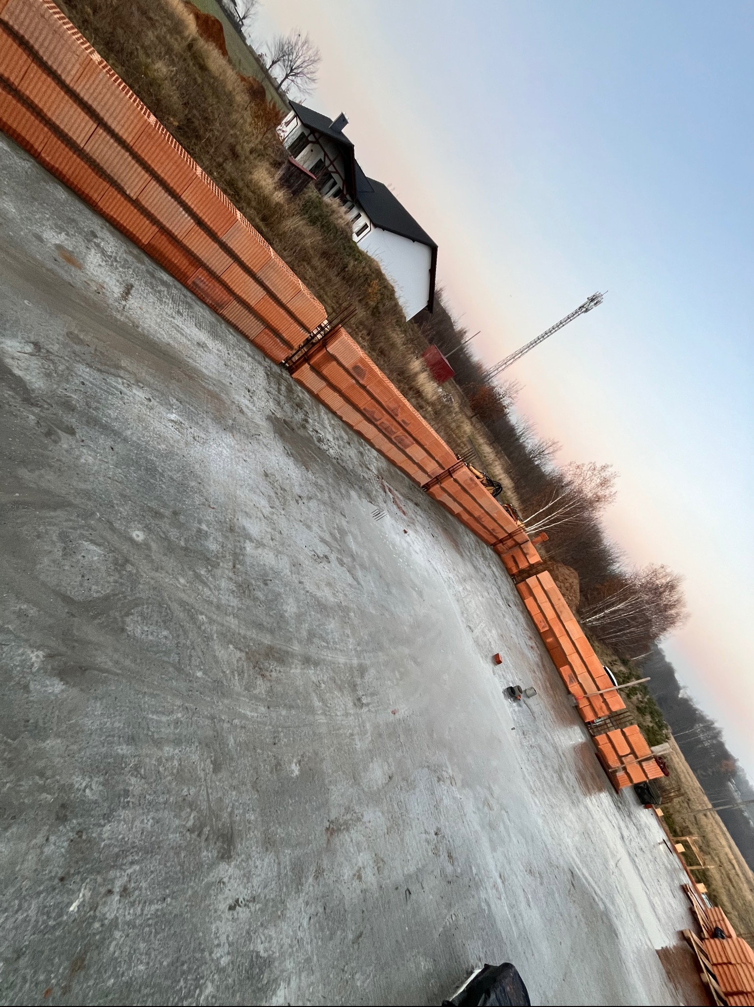 Fundamenty domu z cegły ceramicznej w Przystajni, widok z góry na mokry beton i częściowo wymurowane ściany parteru.