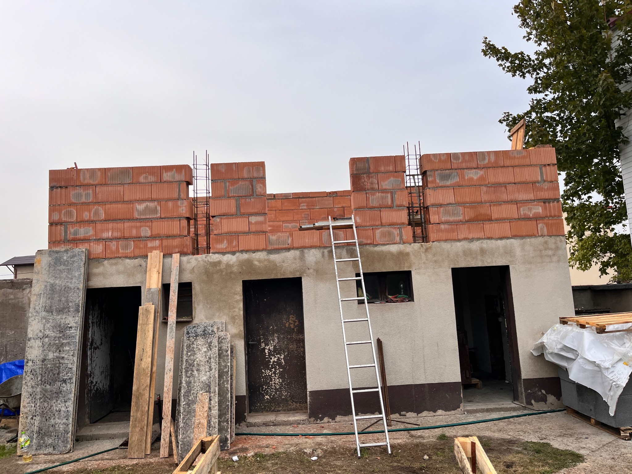 Wznoszenie ścian z czerwonej ceramiki poryzowanej na parterowym budynku, widoczna drabina oparta o ścianę, zbrojenie pionowe w spoinach.