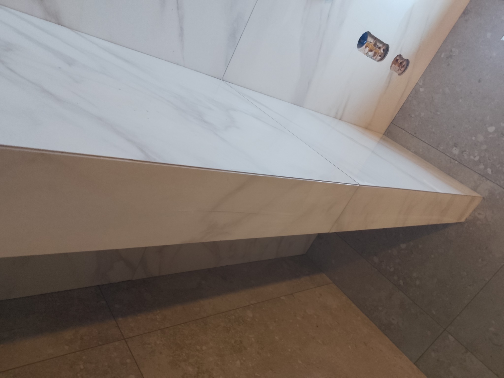 Fragment ściany i podłogi wyłożonych płytkami imitującymi marmur, widoczne puszki elektryczne przed montażem osprzętu.