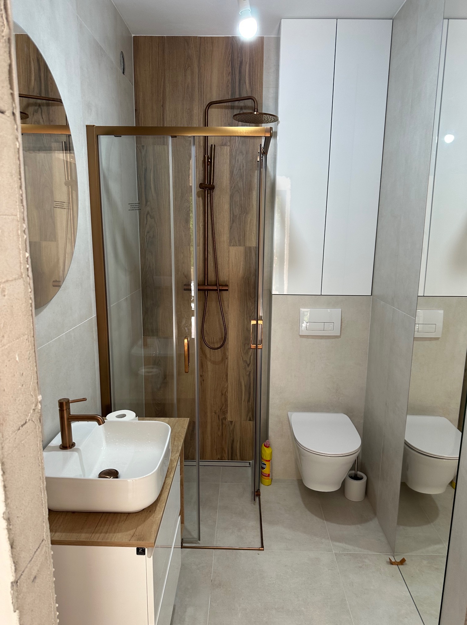 Nowoczesna łazienka z kabiną prysznicową w odcieniach beżu i brązu. Umywalka nablatowa, toaleta i szafki wiszące. Widoczne detale wykończenia.