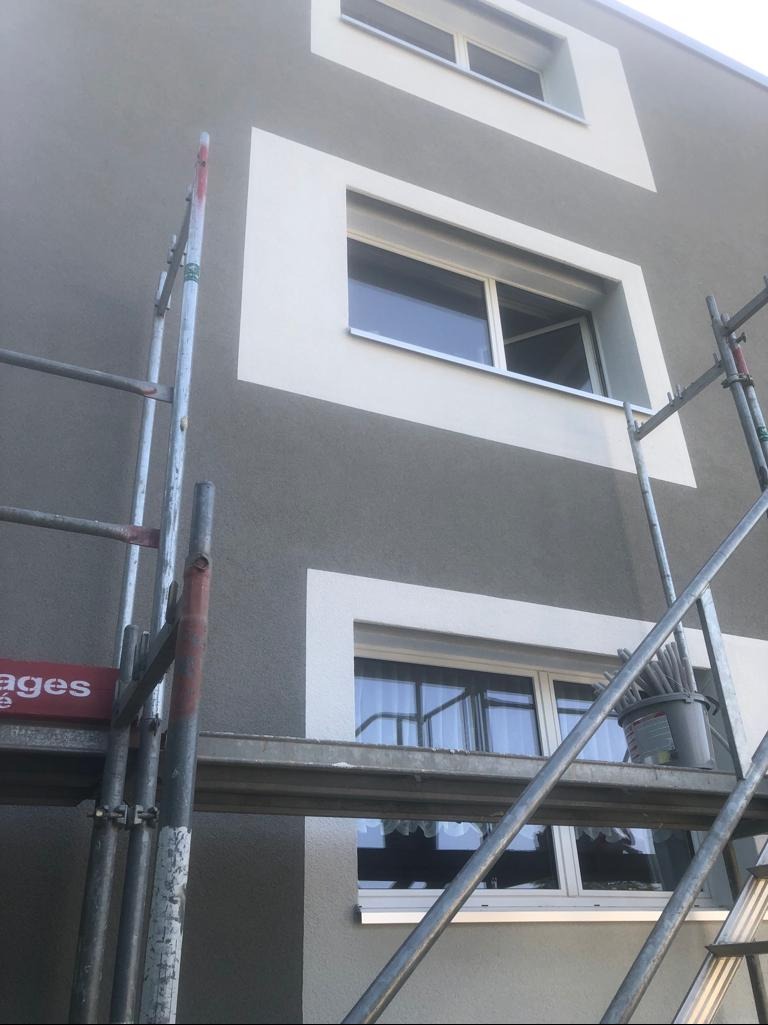 Elewacja budynku po malowaniu, z widocznymi rusztowaniami i oknami z białymi obramowaniami. Świeżo pomalowana fasada na szaro, z elementami dekoracyjnymi.