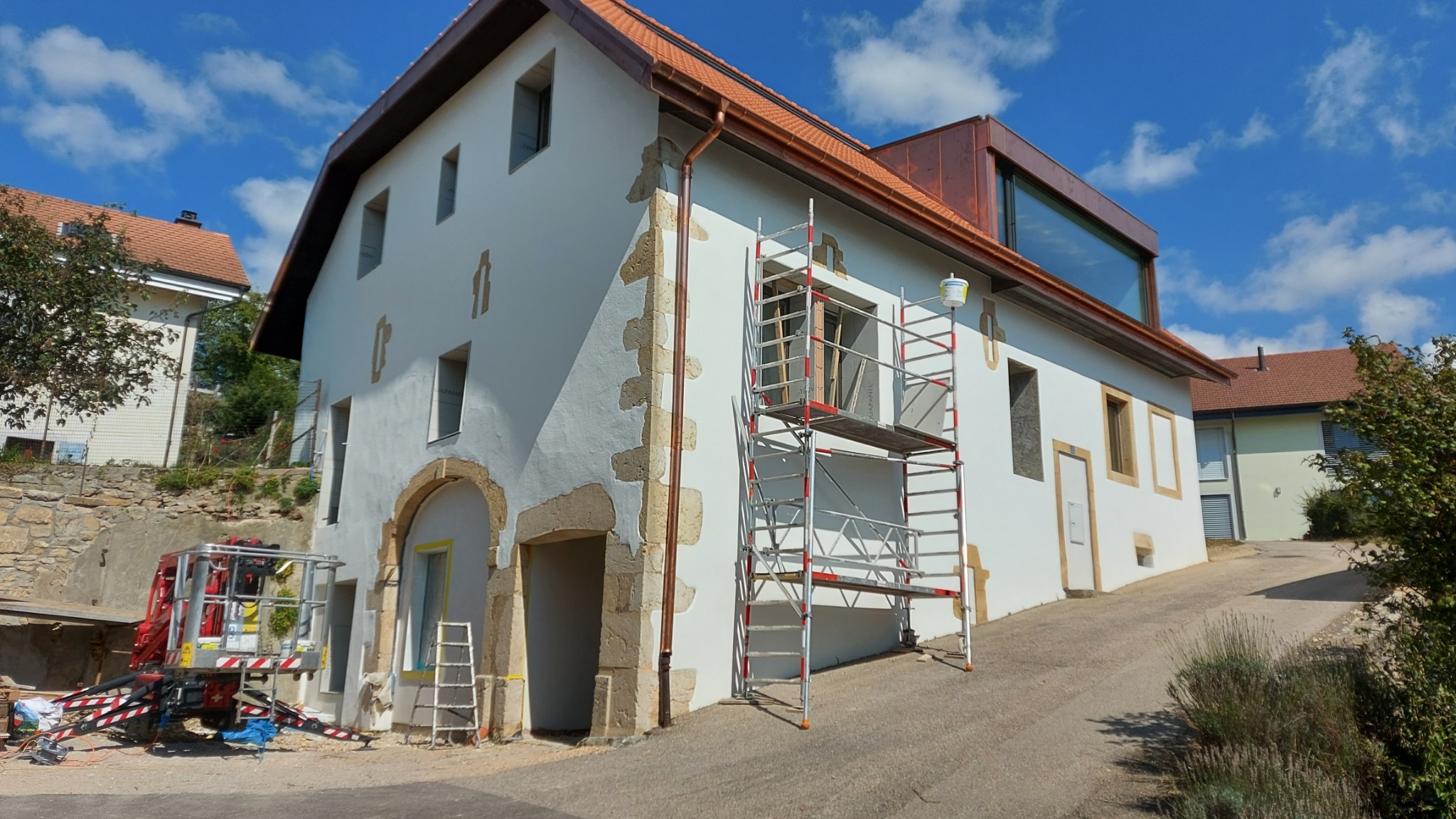 Renowacja elewacji budynku w Miączynie: rusztowanie przy białej ścianie z kamiennymi detalami. Widoczny podnośnik koszowy i przygotowania do prac.