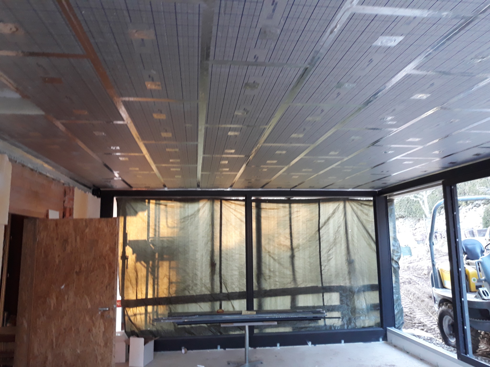 Ocieplenie sufitu z widoczną siatką i elementami mocującymi, przygotowane do dalszych prac wykończeniowych w jasnym pomieszczeniu z widokiem na zewnątrz.