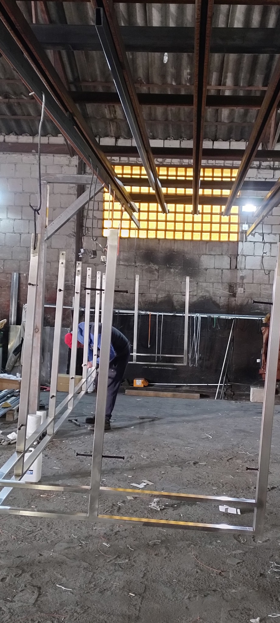 Spawanie konstrukcji ze stali nierdzewnej w warsztacie, widoczne elementy balustrady i spawacz w trakcie pracy, ceglana ściana w tle.