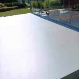 Jasna, gładka posadzka w przeszklonym pomieszczeniu z widokiem na zielony ogród, nowoczesny design.