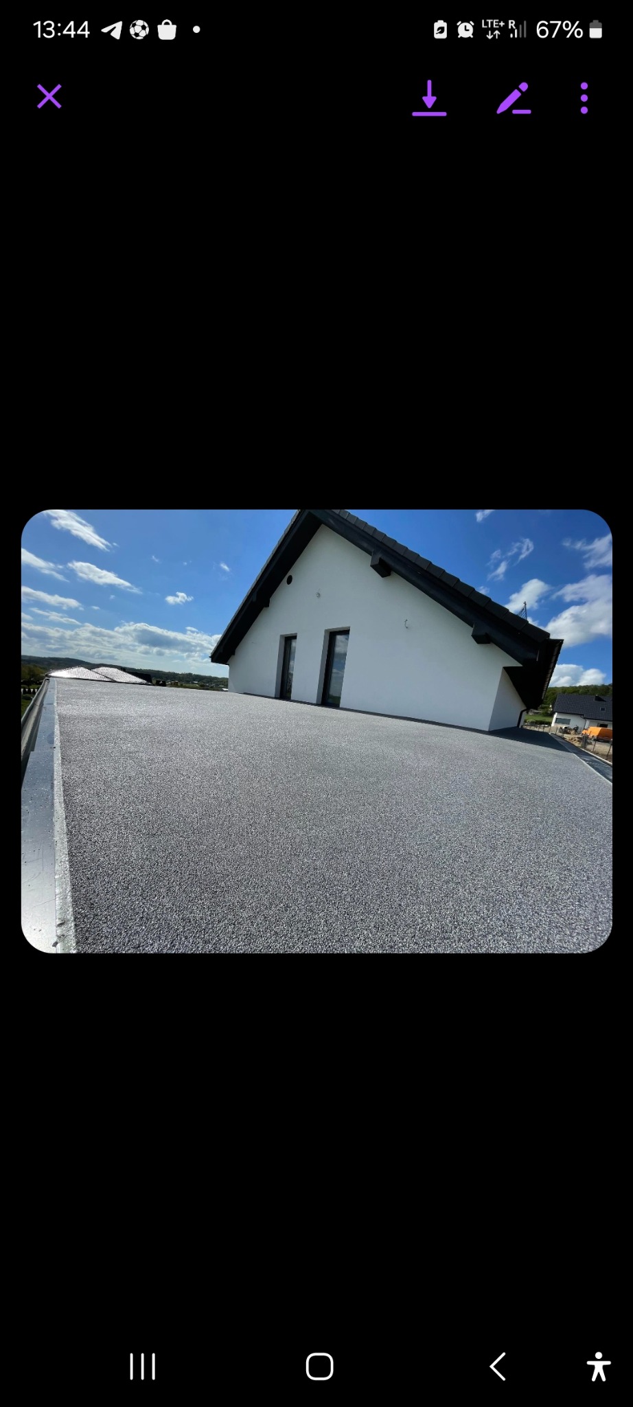 Szara posadzka żywiczna na płaskim dachu domu jednorodzinnego z widocznymi dwoma oknami dachowymi i fragmentem krajobrazu w tle.