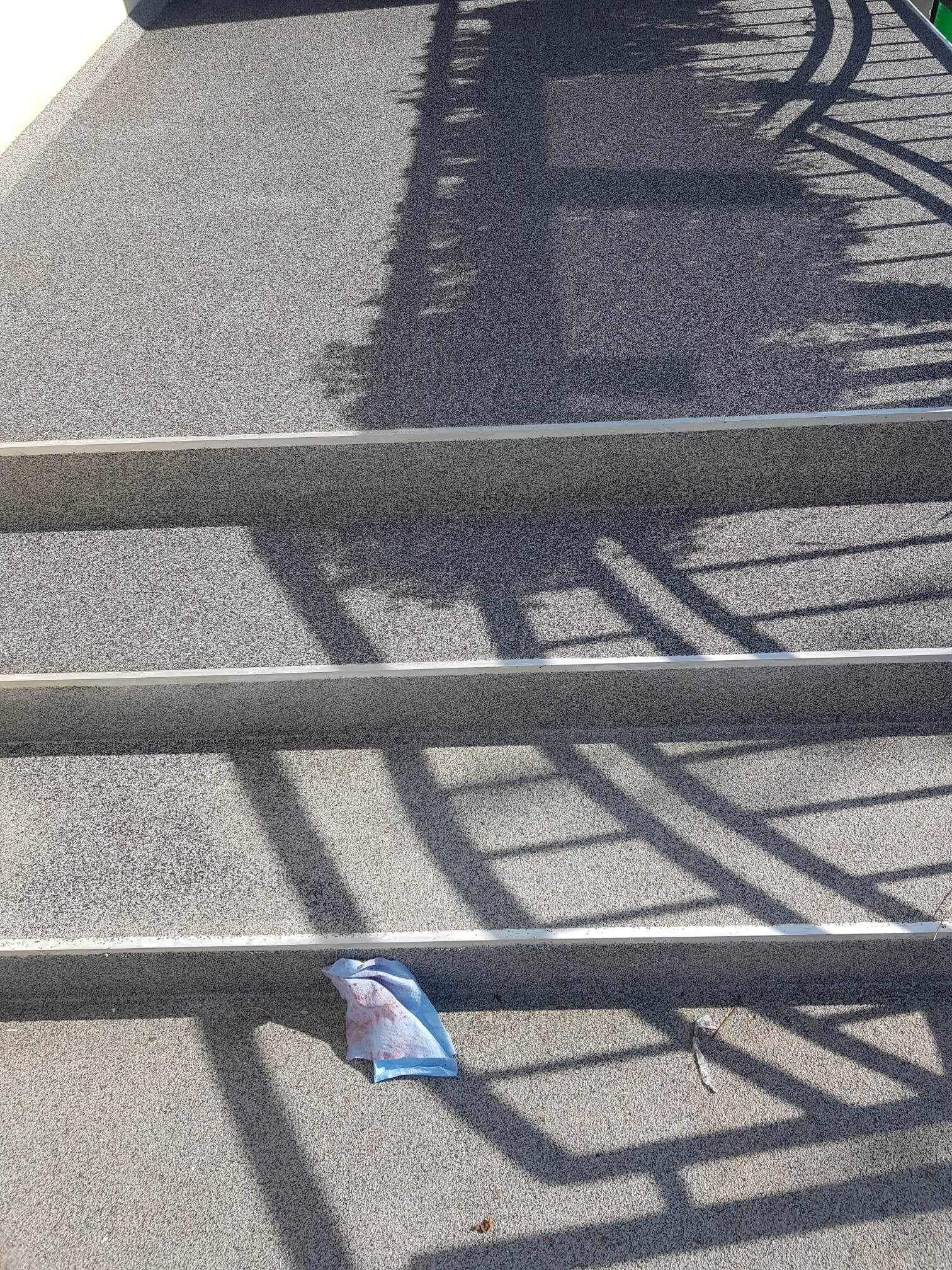 Schody z szarej posadzki żywicznej z widocznymi cieniami balustrady i leżącą szmatką na jednym ze stopni.