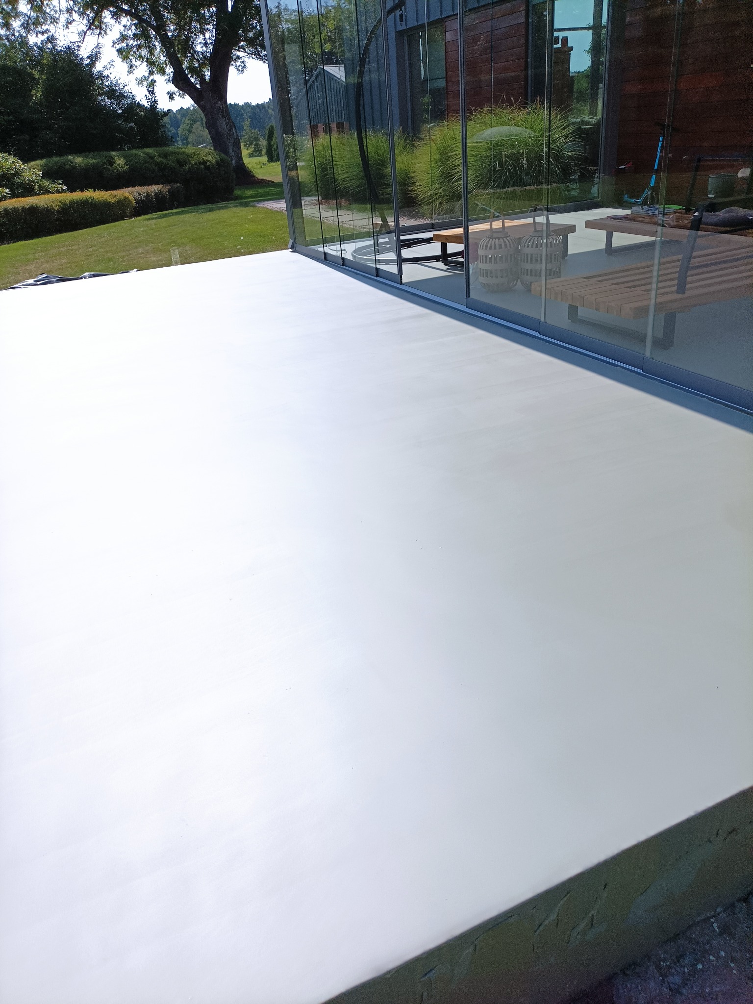 Jasna, gładka posadzka w przeszklonym pomieszczeniu z widokiem na zielony ogród, nowoczesny design.