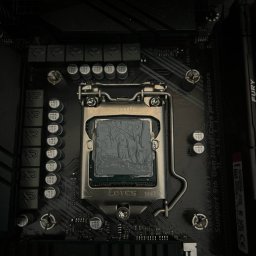 P-cet - Płyta główna z zamontowanym procesorem Intel, pokrytym pastą termoprzewodzącą, gotowa do montażu chłodzenia. Widoczne elementy płyty głównej i gniazdo procesora.