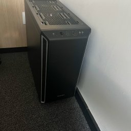 P-cet - Czarna obudowa komputera stacjonarnego marki be quiet! ustawiona pionowo na ciemnej wykładzinie, widoczne porty USB i przycisk zasilania na górnym panelu.