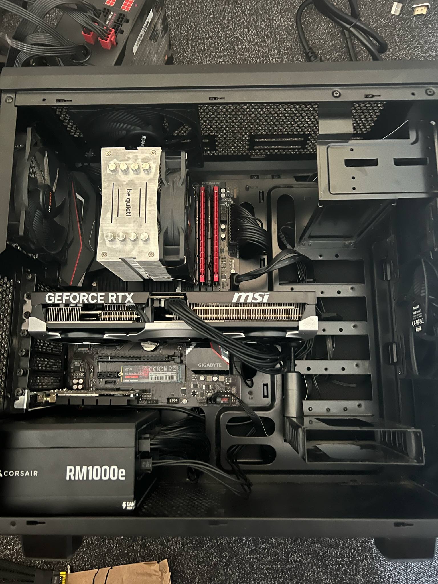 Wnętrze obudowy komputera stacjonarnego z kartą graficzną GeForce RTX, chłodzeniem be quiet!, płytą główną MSI i zasilaczem Corsair RM1000e. Widoczne kable i komponenty.