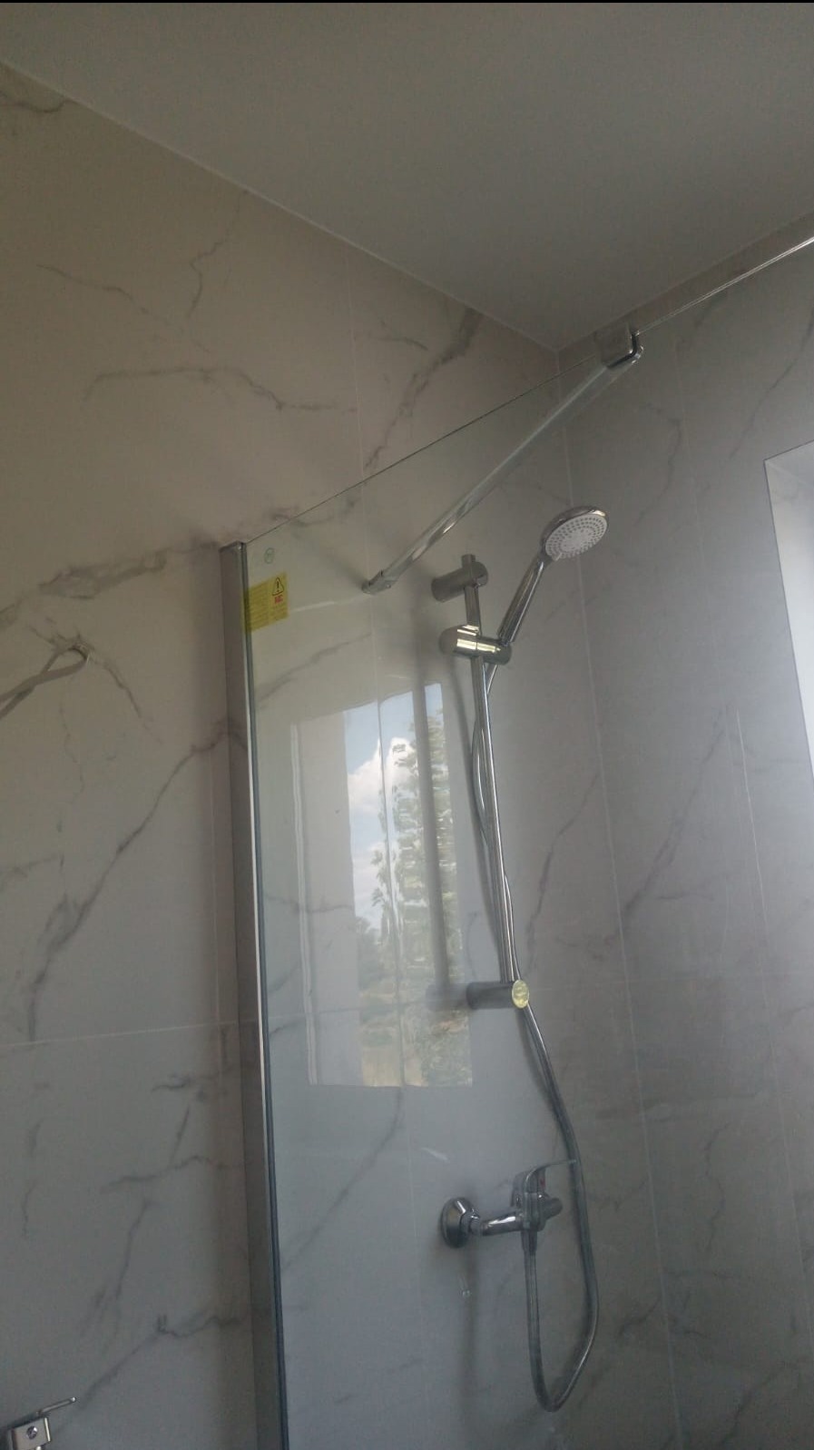 Nowoczesna kabina prysznicowa z chromowaną armaturą, zamontowana na ścianie wyłożonej płytkami imitującymi marmur, widok od dołu.