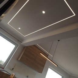 S.perfect-tech Paweł Sperczyński - Nowoczesne oświetlenie sufitowe z liniami LED tworzącymi prostokąt, uzupełnione punktowymi lampami. W tle widoczne zabudowy meblowe i okno.