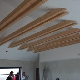 S.perfect-tech Paweł Sperczyński - Drewniane belki dekoracyjne zamontowane pod sufitem w surowym wnętrzu, widoczni pracownicy w tle.