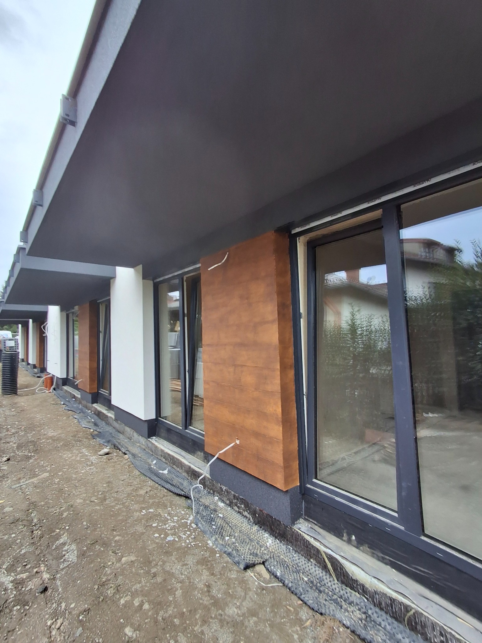 Elewacja budynku z drewnopodobnymi panelami i szarym wykończeniem, widok z dołu, ukazujący detale montażu i wykończenia.