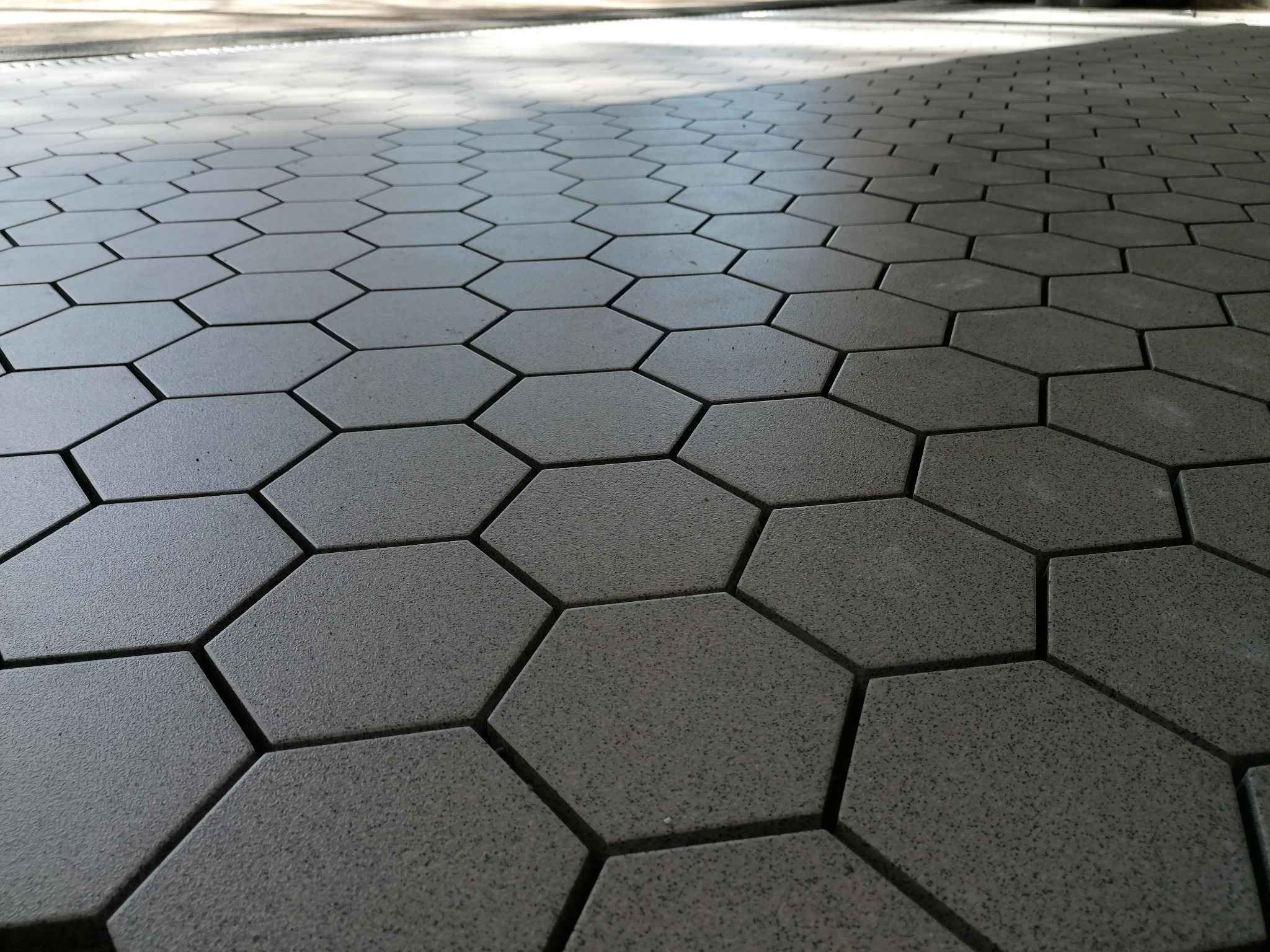 Szara, sześciokątna kostka brukowa ułożona na powierzchni, widok z niskiej perspektywy z lekkim cieniem u góry.