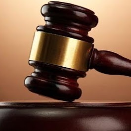 Drewniany młotek sędziowski z pozłacanym elementem na stole, ciemnobrązowa podstawa, ciepłe, rozproszone światło.