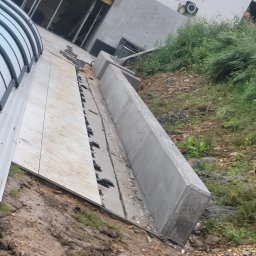 KIRBUD Krzysztof Kirkiewicz - Przygotowanie podłoża pod wylewkę z widocznymi elementami szalunku, mocowaniami i fragmentem budynku w tle.