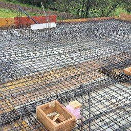 KIRBUD Krzysztof Kirkiewicz - Zbrojenie płyty fundamentowej z siatki stalowej, drewniane szalunki obwodowe i skrzynki na tle zieleni.