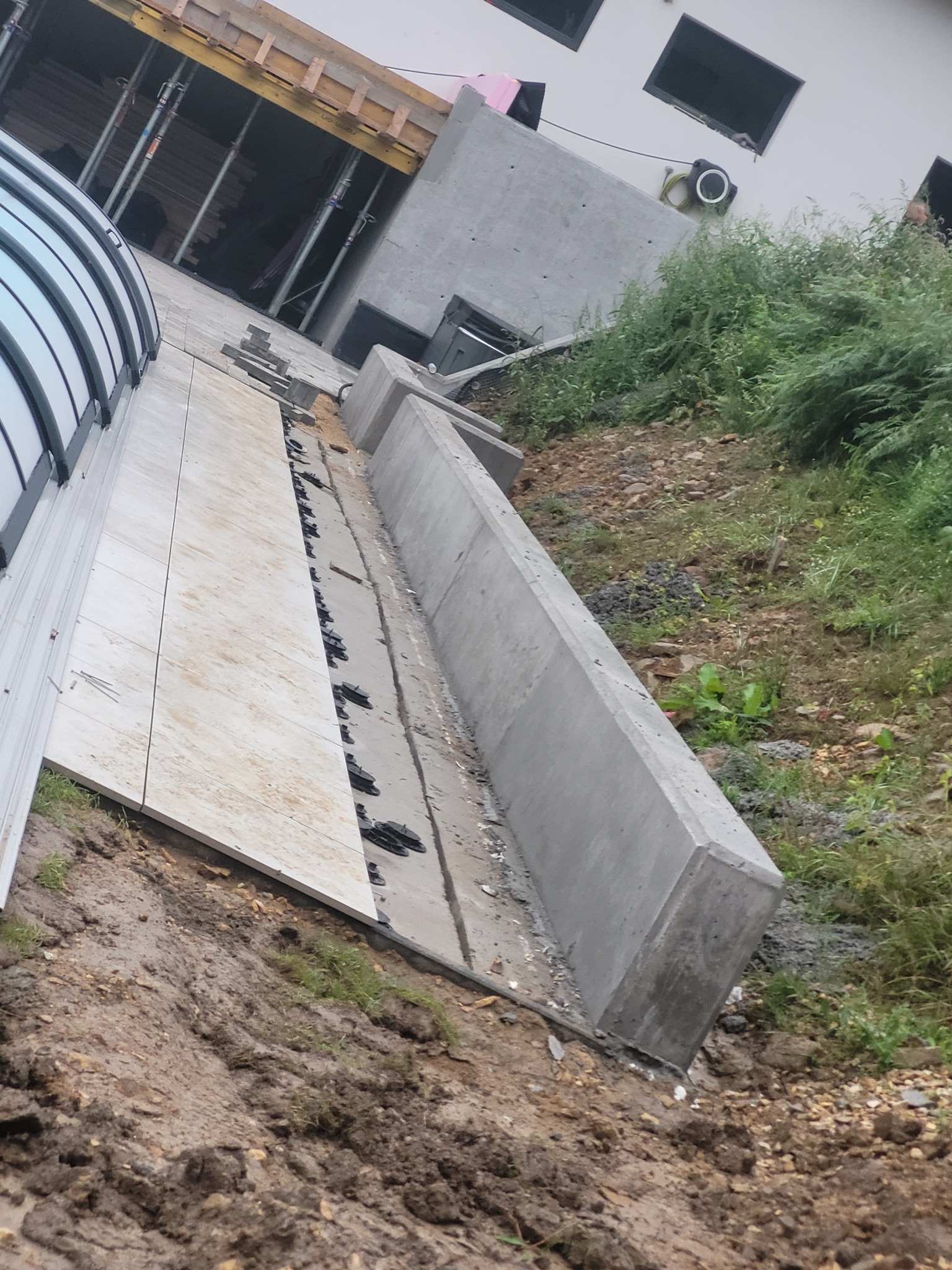 Przygotowanie podłoża pod wylewkę z widocznymi elementami szalunku, mocowaniami i fragmentem budynku w tle.